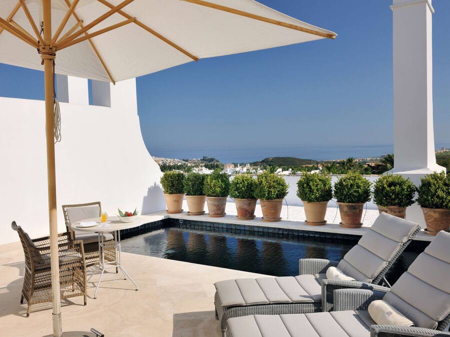 A poolside area with lounge chairs, a table, and potted plants.