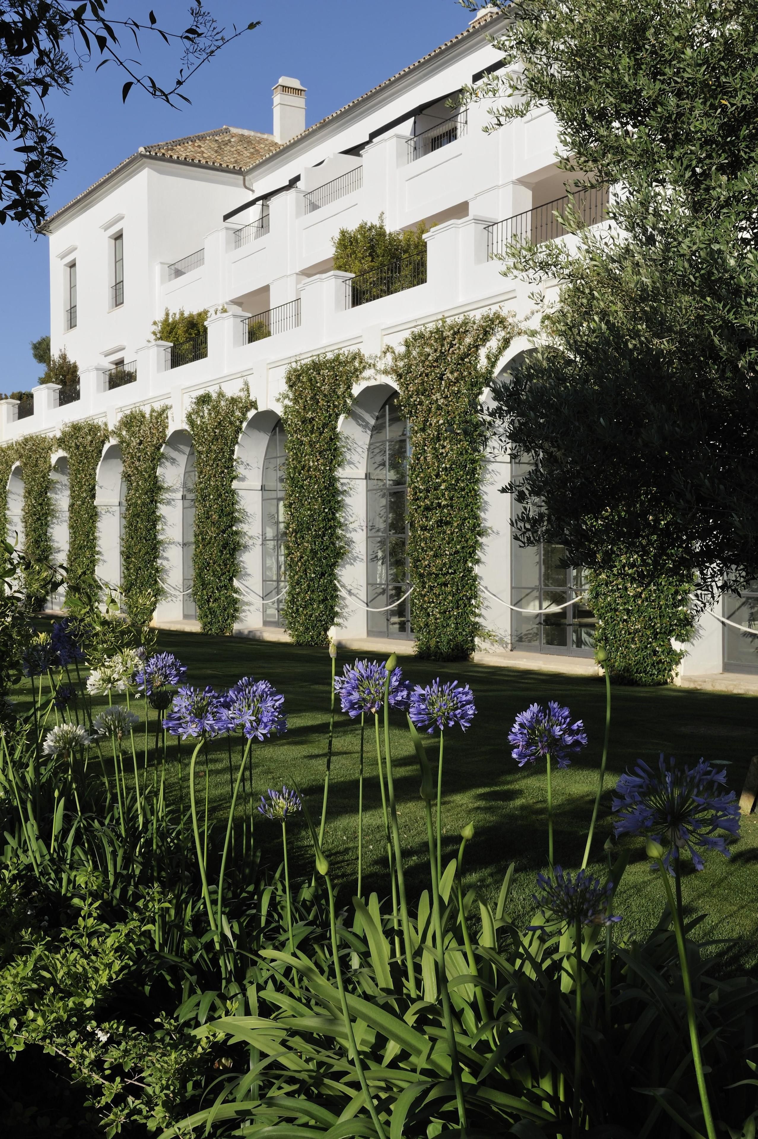 A white building with multiple balconies, a well-maintained lawn, and flowering plants.