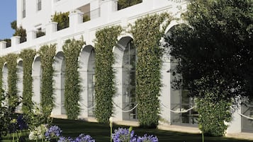 A white building with multiple balconies, a well-maintained lawn, and flowering plants.
