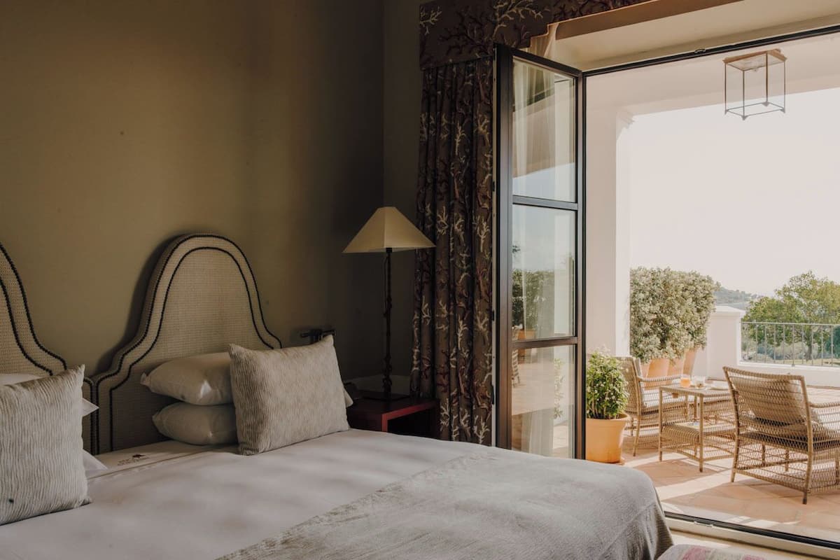 Un dormitorio con una cama grande, una mesita de noche, una lámpara y vistas a un patio exterior con sillas y una mesa.