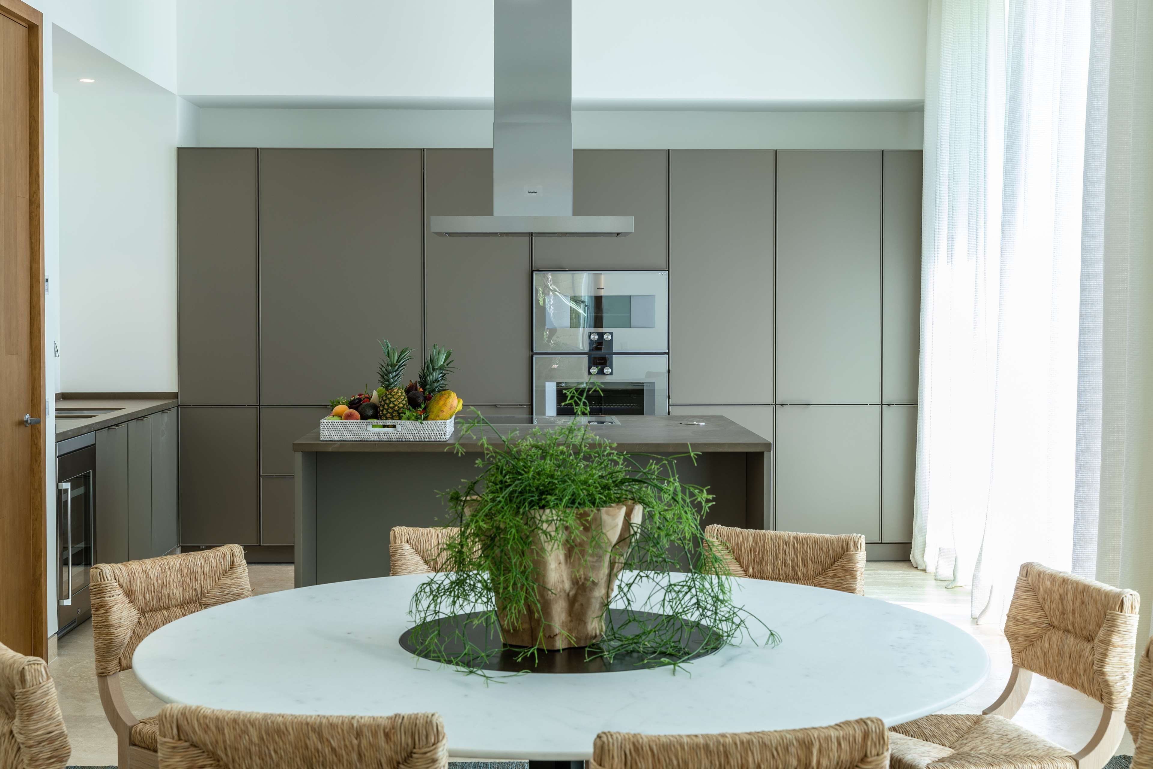 A modern kitchen with a central island, built-in appliances, and a dining area with wicker chairs.