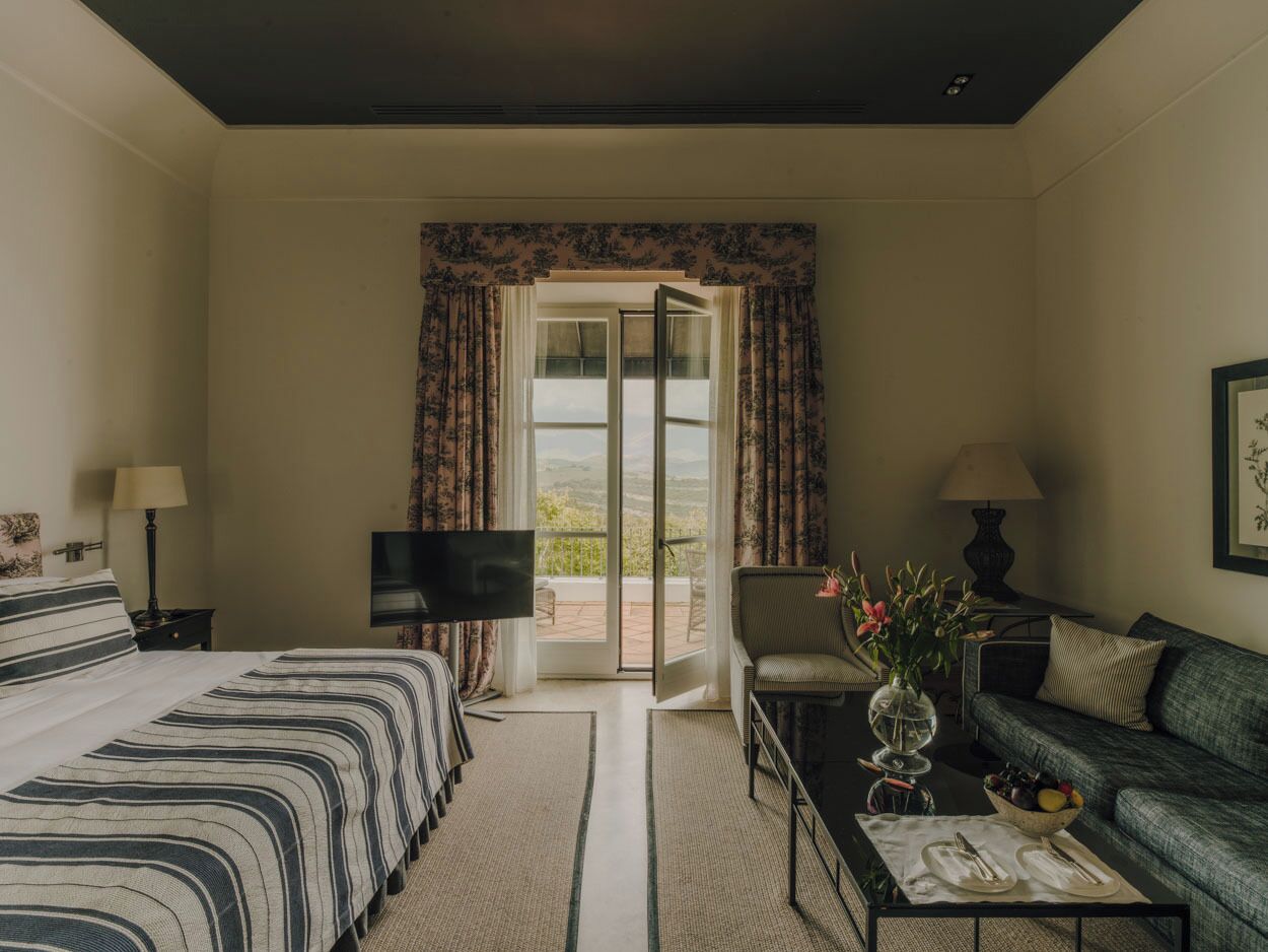 A hotel room with a bed, a sofa, a TV, a coffee table, and a view through a glass door.