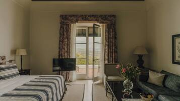 A hotel room with a bed, a sofa, a TV, a coffee table, and a view through a glass door.