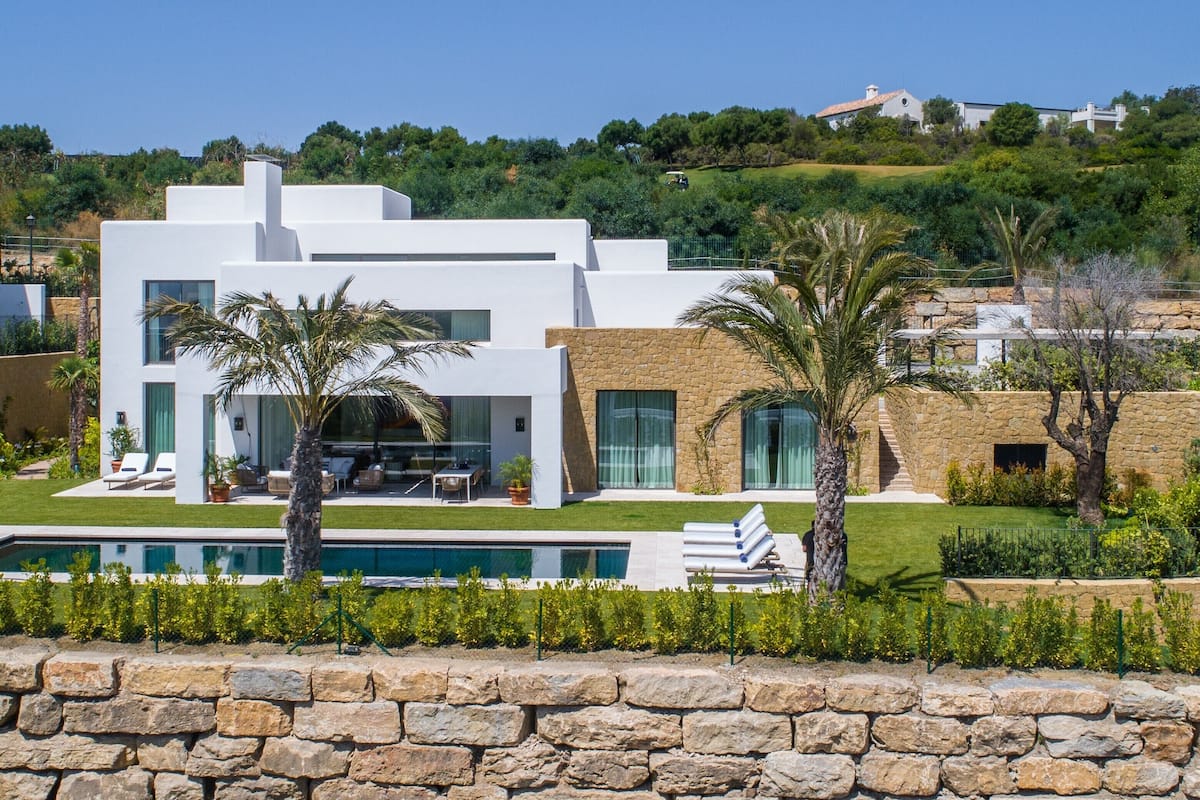 Una casa moderna de dos pisos con piscina, muros de piedra y abundante vegetación.