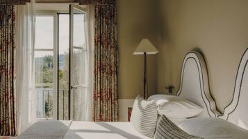 Habitación de hotel con cama, mesita de noche, lámpara y vista a través de una ventana con cortinas.