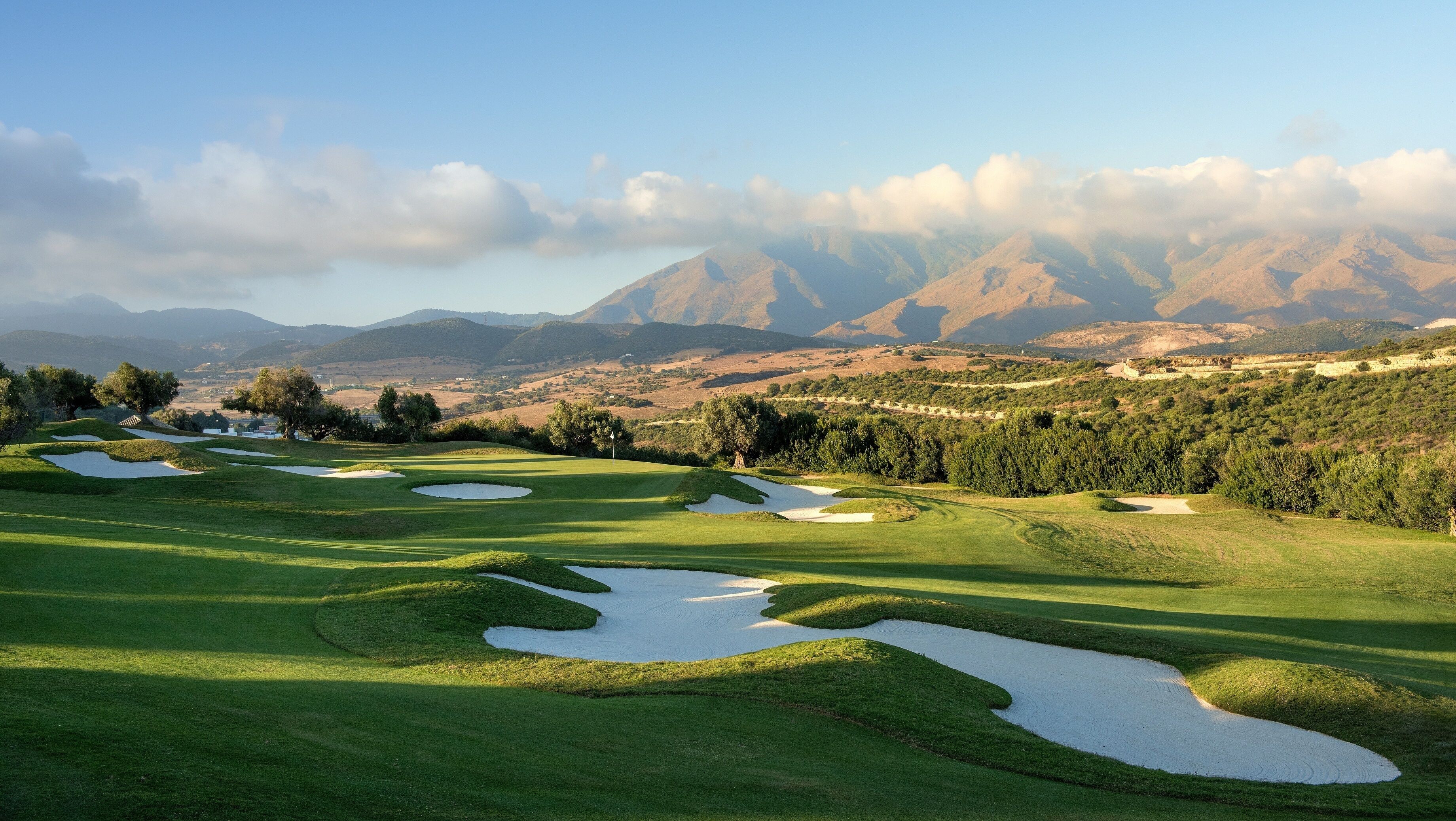 A golf course with sand bunkers and a mountainous backdrop.