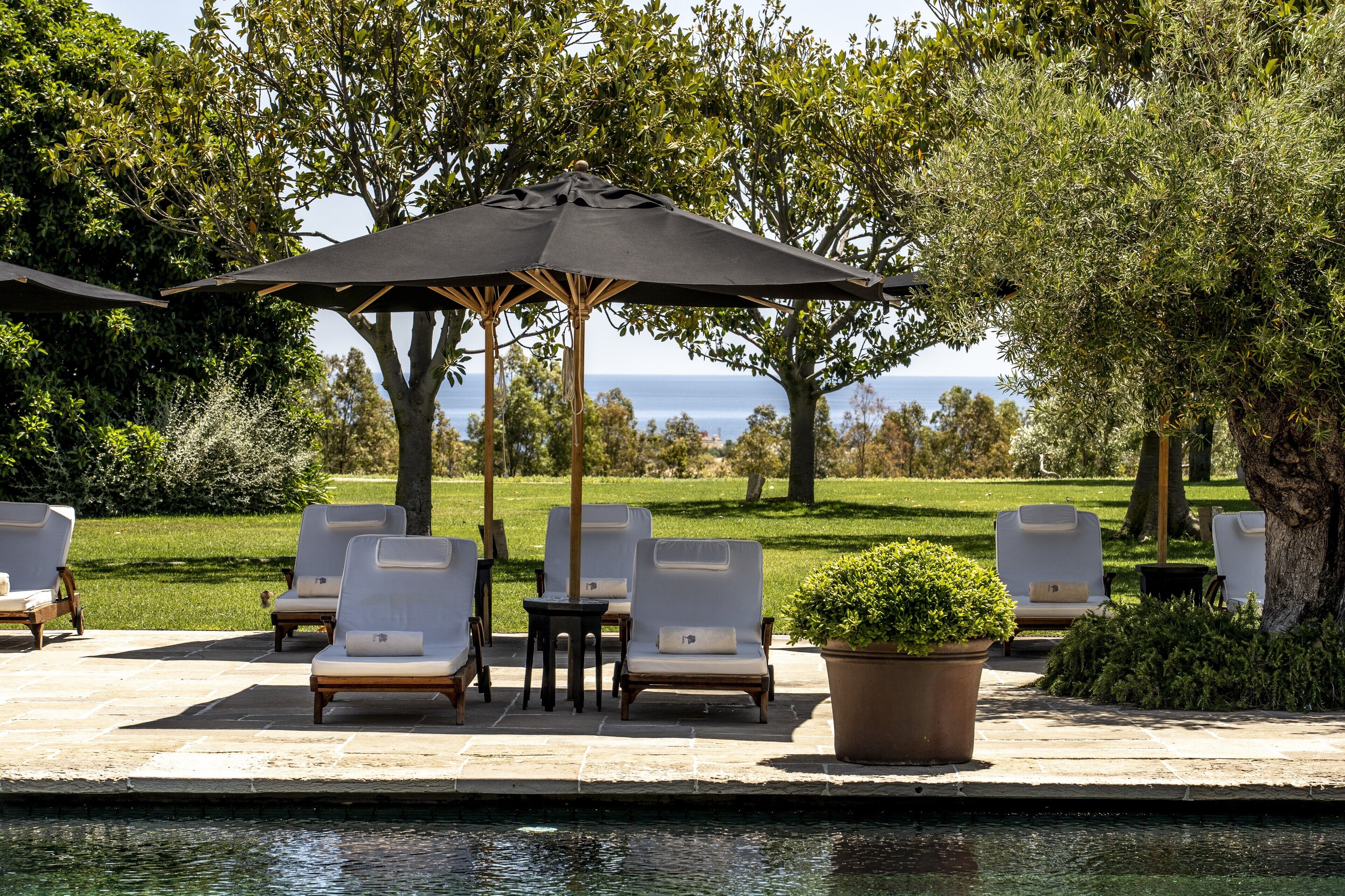 Zona junto a la piscina con sillones de descanso, una mesa y una sombrilla.