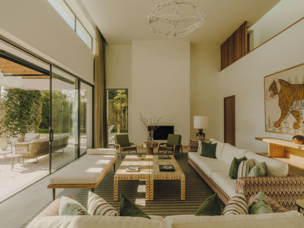 Una sala de estar moderna con un conjunto de sofá, una mesa de centro, sillas, un televisor de pantalla plana y un ventanal con vistas a la vegetación.