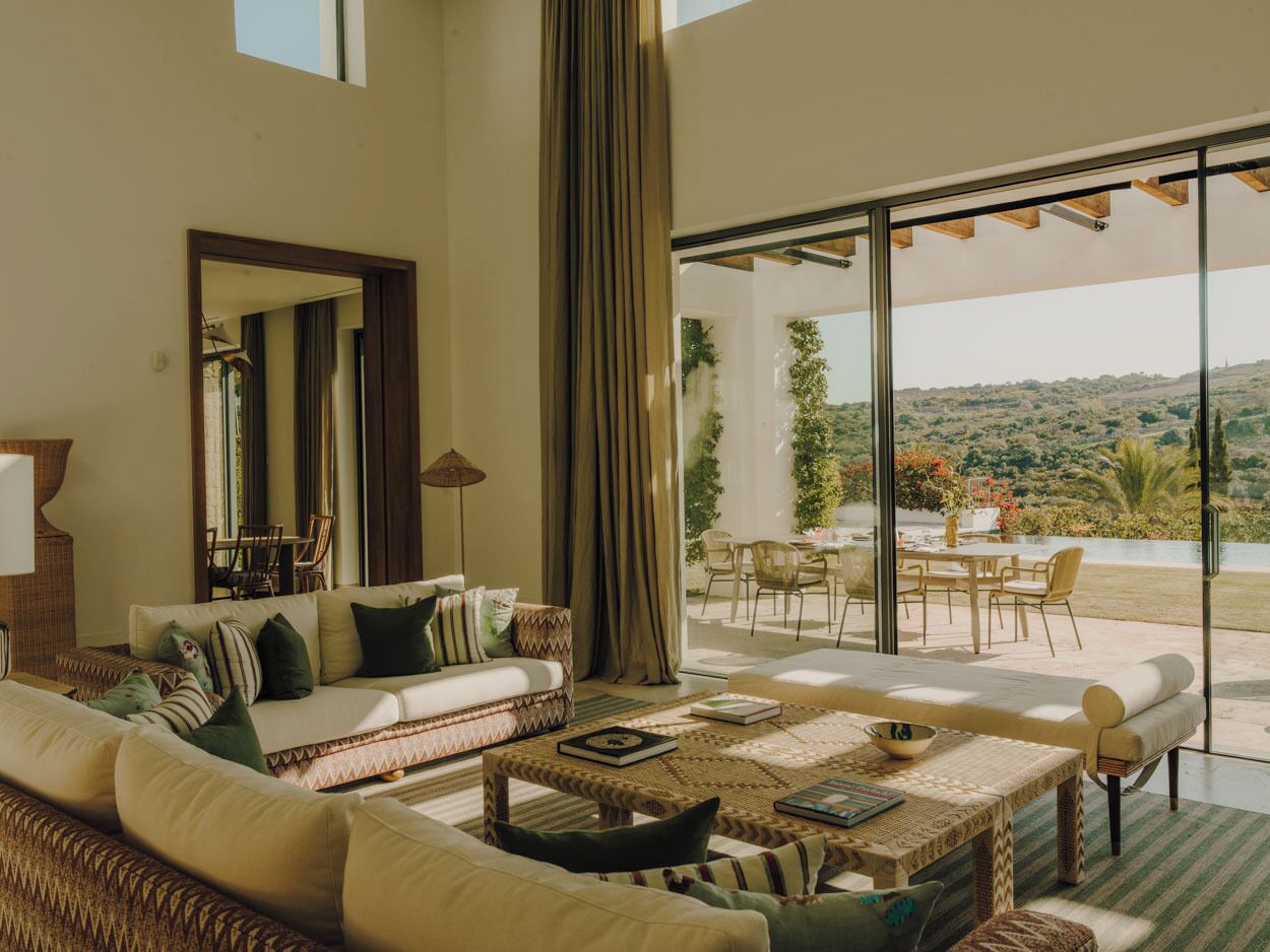 Amplia sala de estar con un sofá grande, una mesa de centro y un juego de comedor. Unas puertas correderas de vidrio dan a un patio exterior con vistas a una colina.