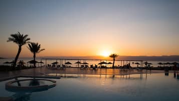 Relax by the serene pool, surrounded by lounge chairs and umbrellas, with a covered walkway offering a shaded area.