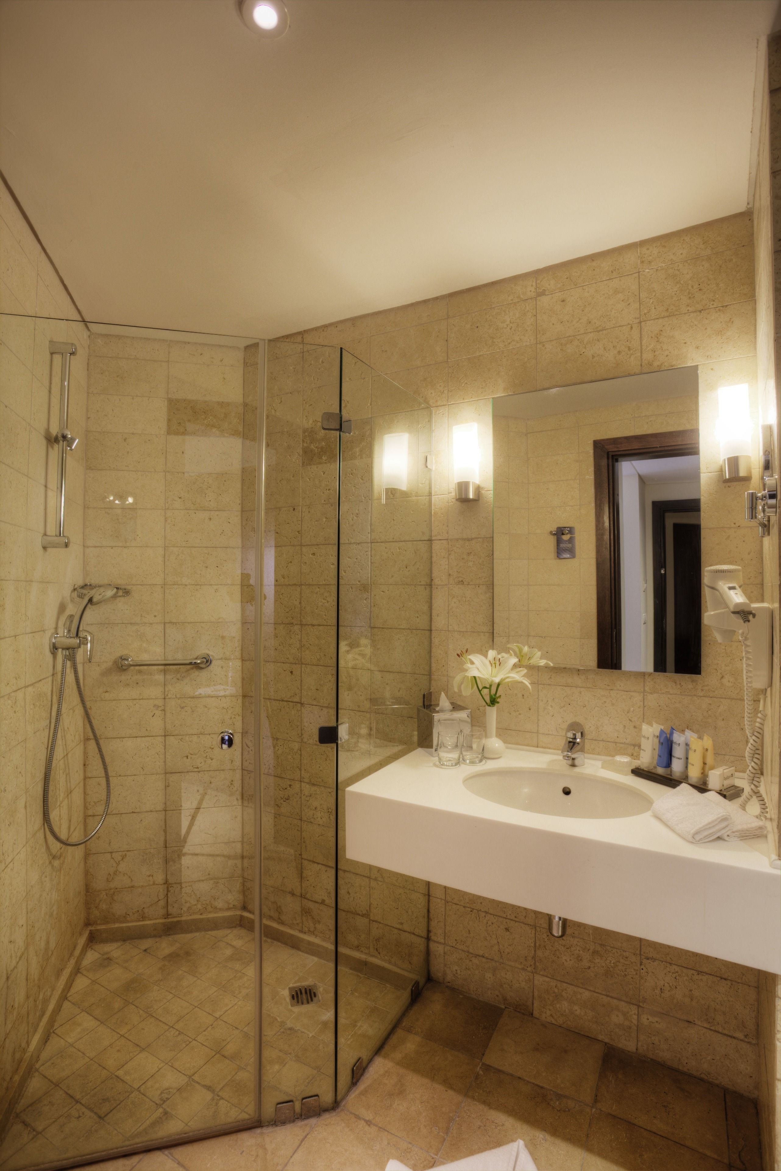 Un baño moderno con ducha de vidrio, un lavabo amplio con espejo y un inodoro.