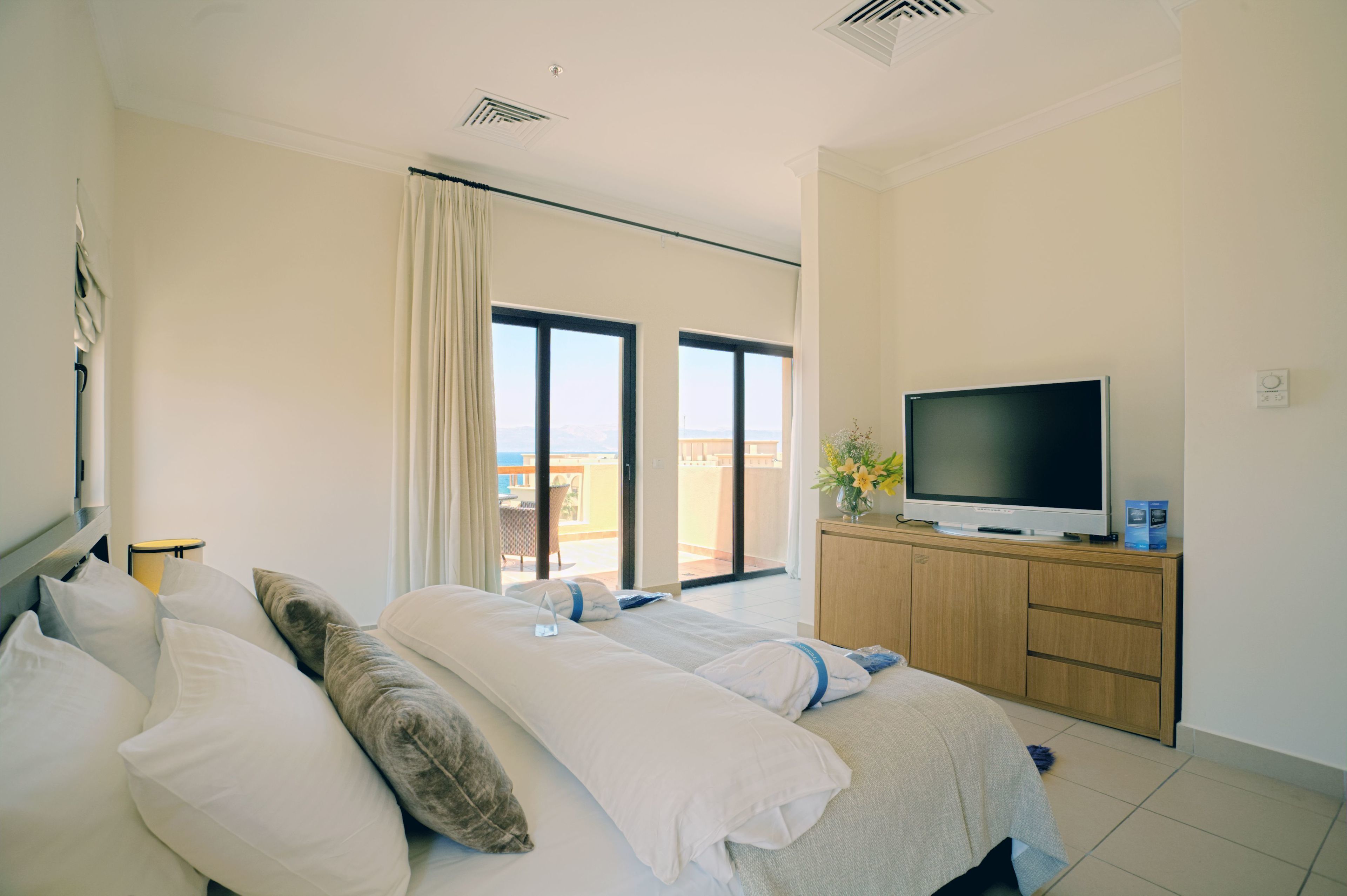 Habitación de hotel con dos camas, un televisor, un balcón con vistas y un armario de madera.