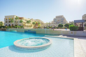 A swimming pool with a hot tub, surrounded by palm trees and buildings with balconies. - Grand Tala Bay Resort, Aqaba (Aqaba)