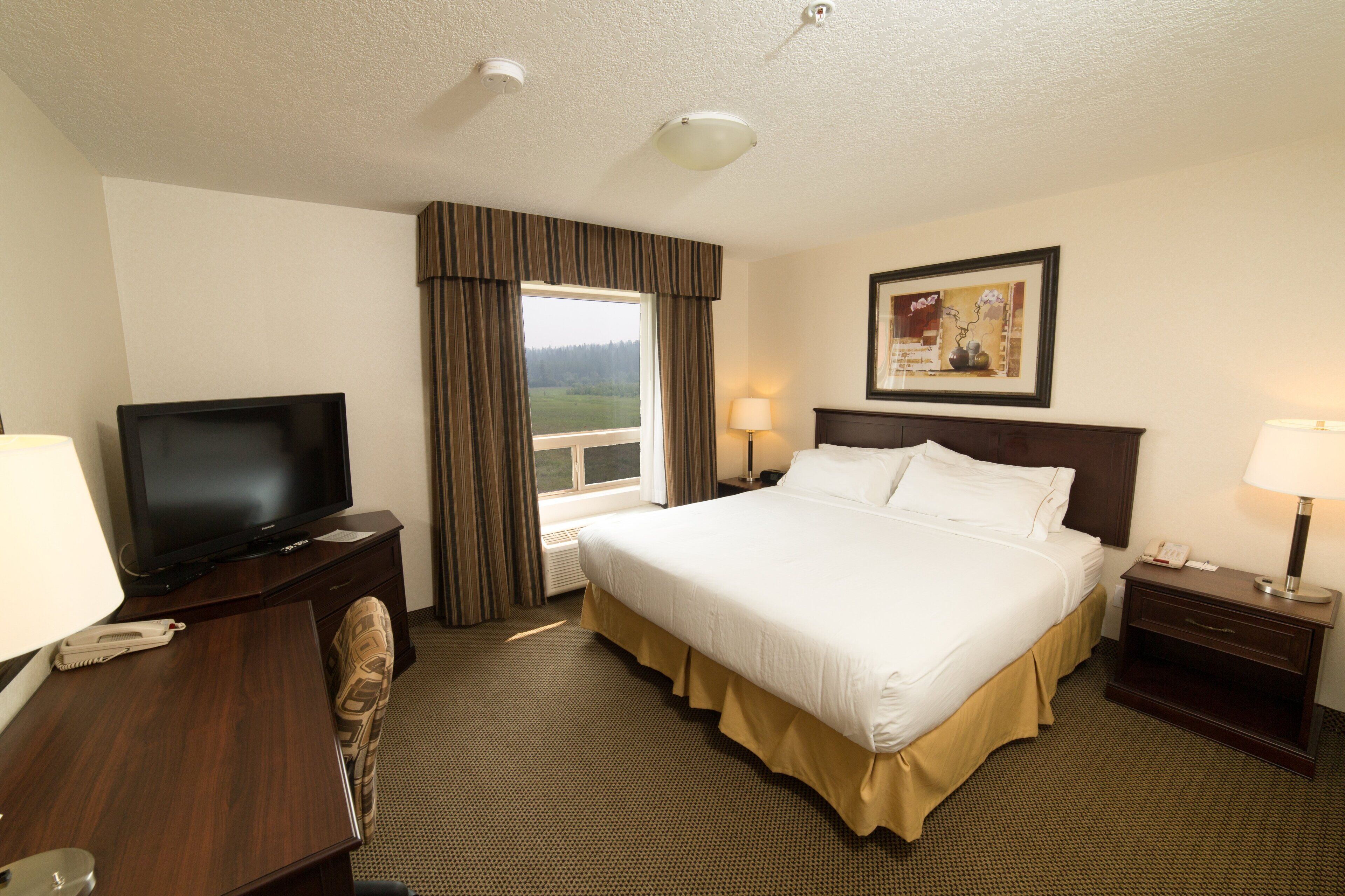 A hotel room with a large bed, a television, a desk with a telephone, and a window with curtains.