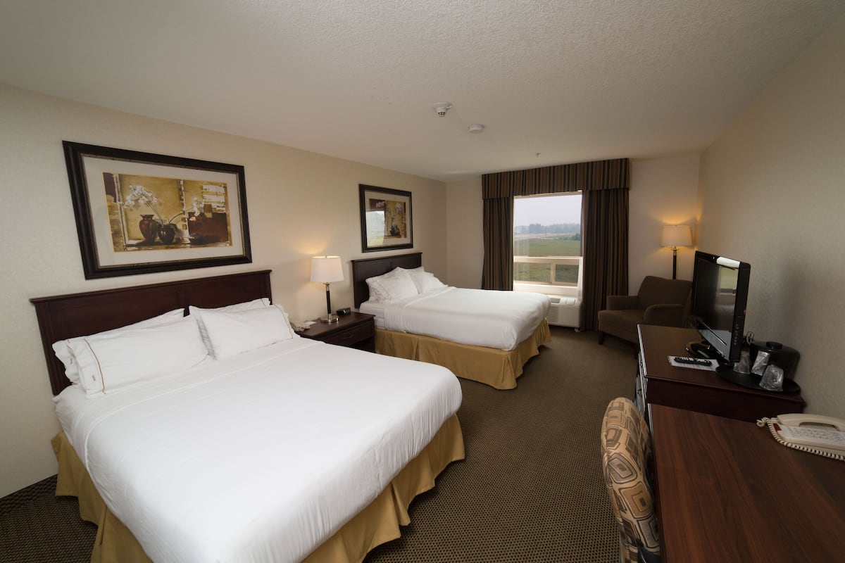 A hotel room with two beds, a desk, a chair, a TV, and a window with curtains.