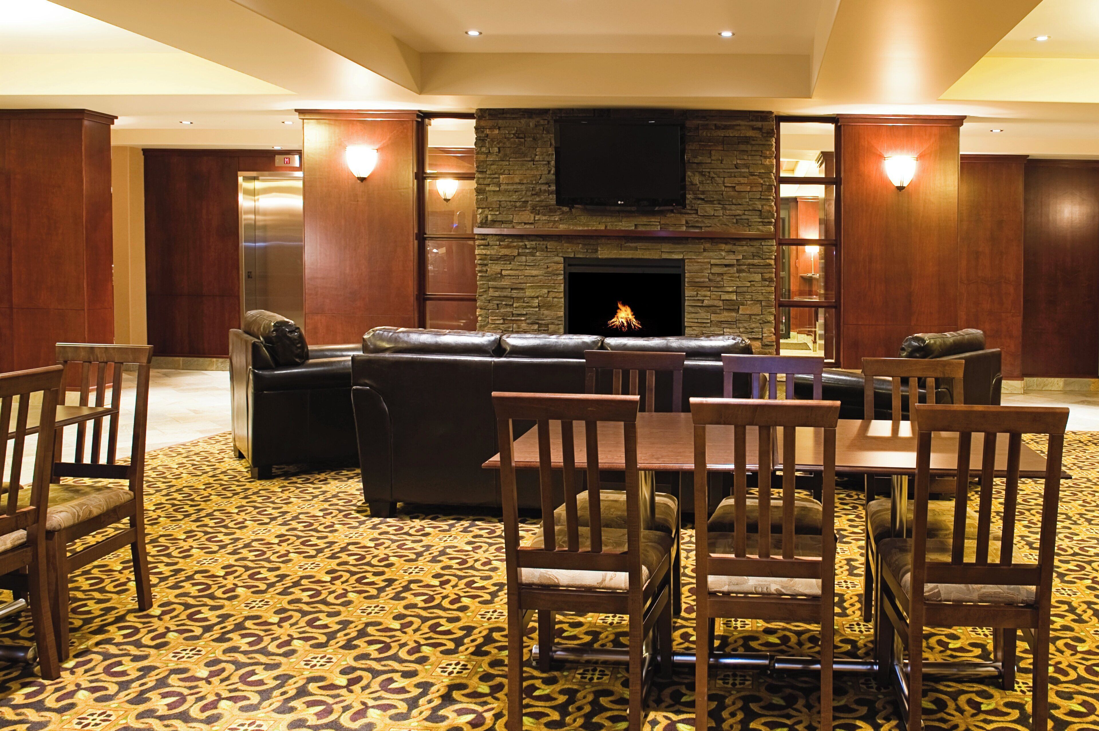 Un vestíbulo de hotel con chimenea, sofás de cuero, sillas de madera y una alfombra estampada.