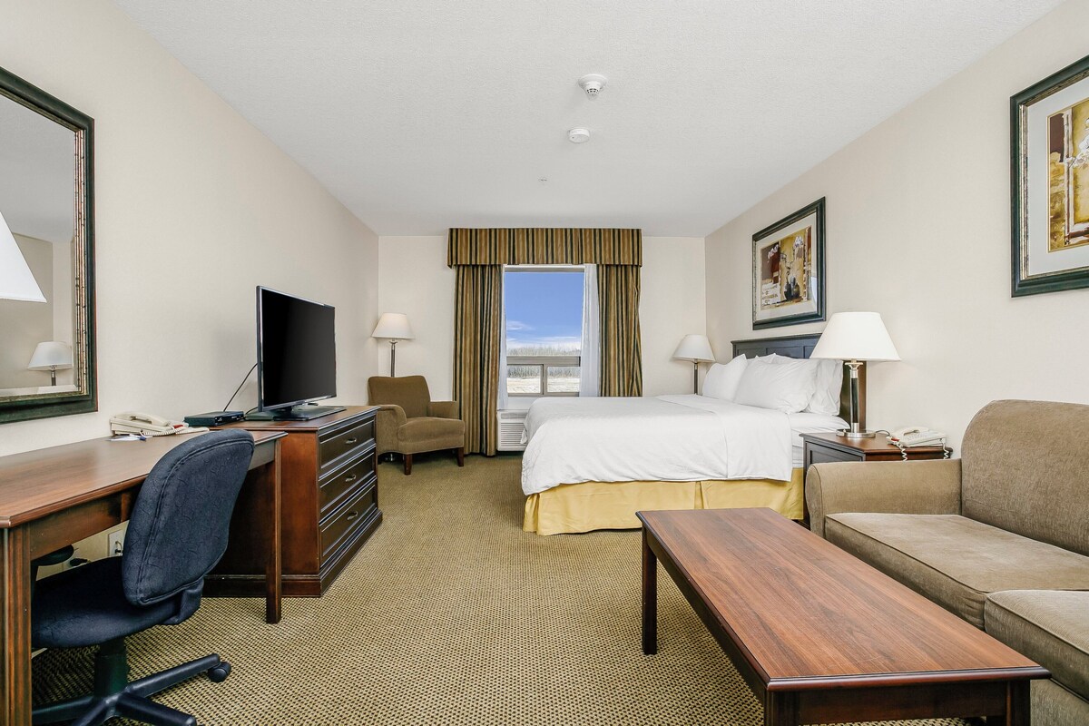 A hotel room with a bed, desk, chair, TV, and a sofa.