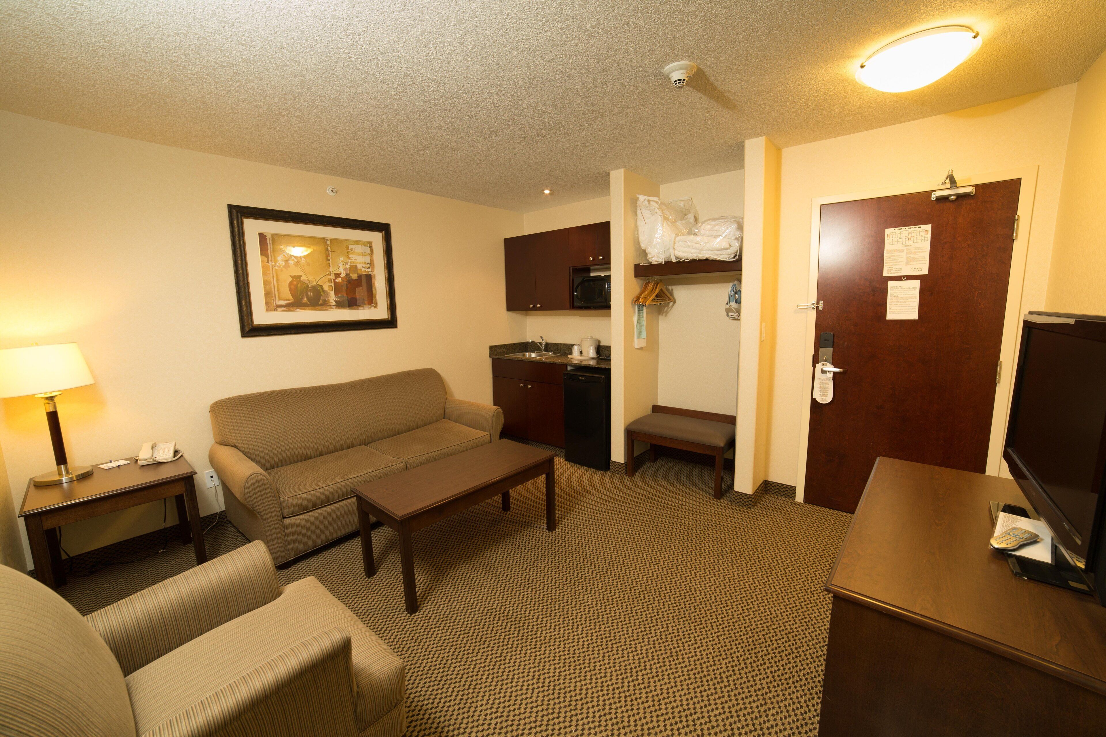 A hotel room with a sofa, a small table, a TV, a desk, a lamp, and a kitchenette.