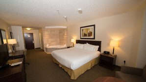 A hotel room with a large bed, a desk with a computer, a chair, a small table, a nightstand with a lamp, and a bathroom with a bathtub and shower. - Holiday Inn Express & Suites Slave Lake by IHG (Slave Lake)