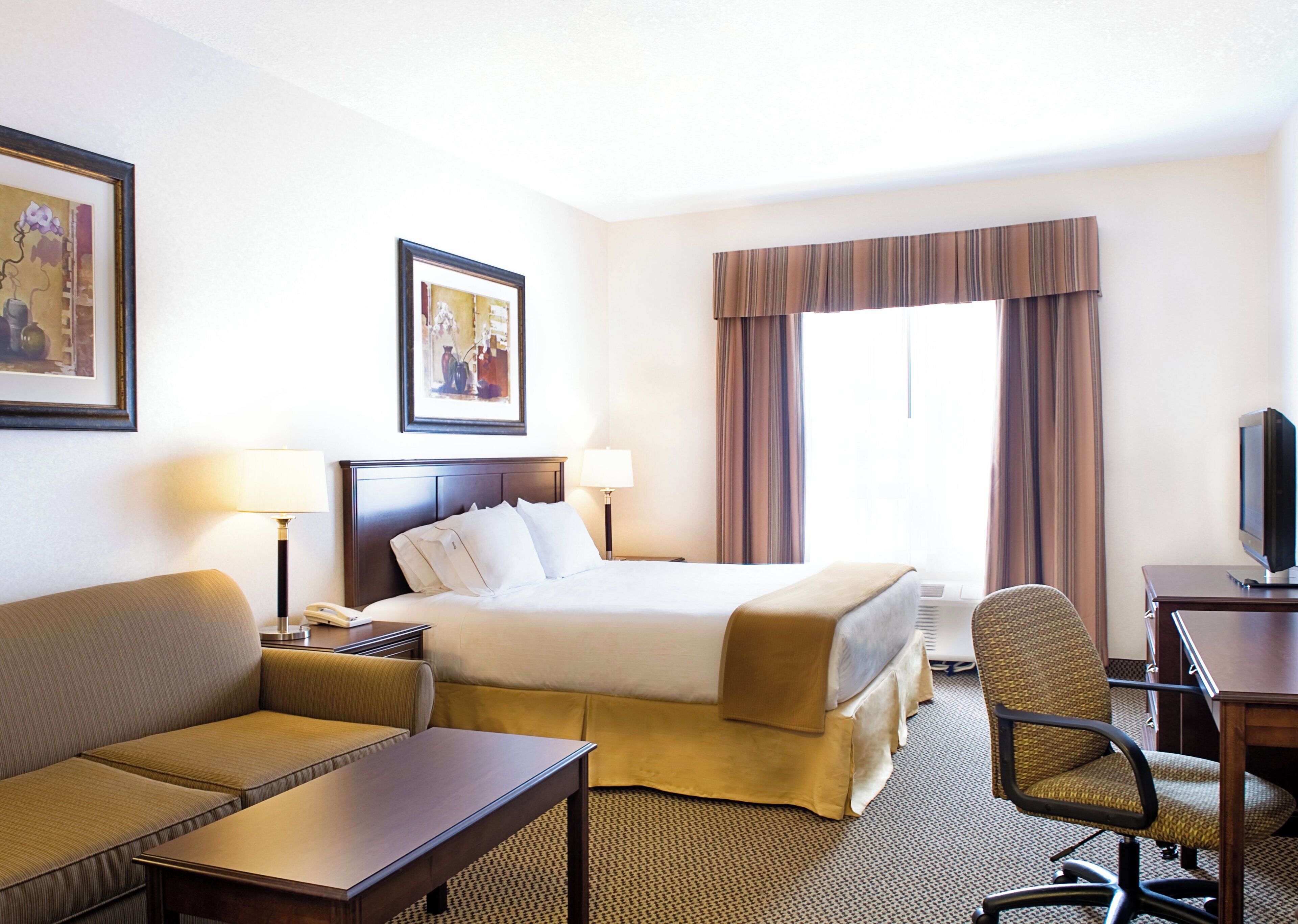 A hotel room with a bed, a sofa, a desk, a chair, a television, and two lamps.