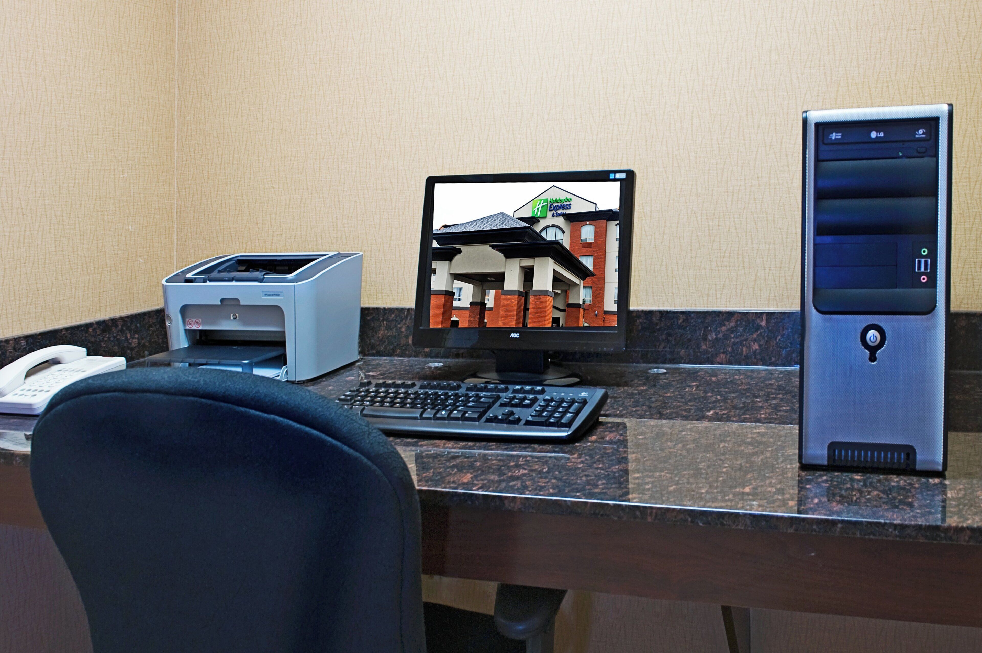 A hotel room with a desktop computer, a printer, and a telephone on the desk.