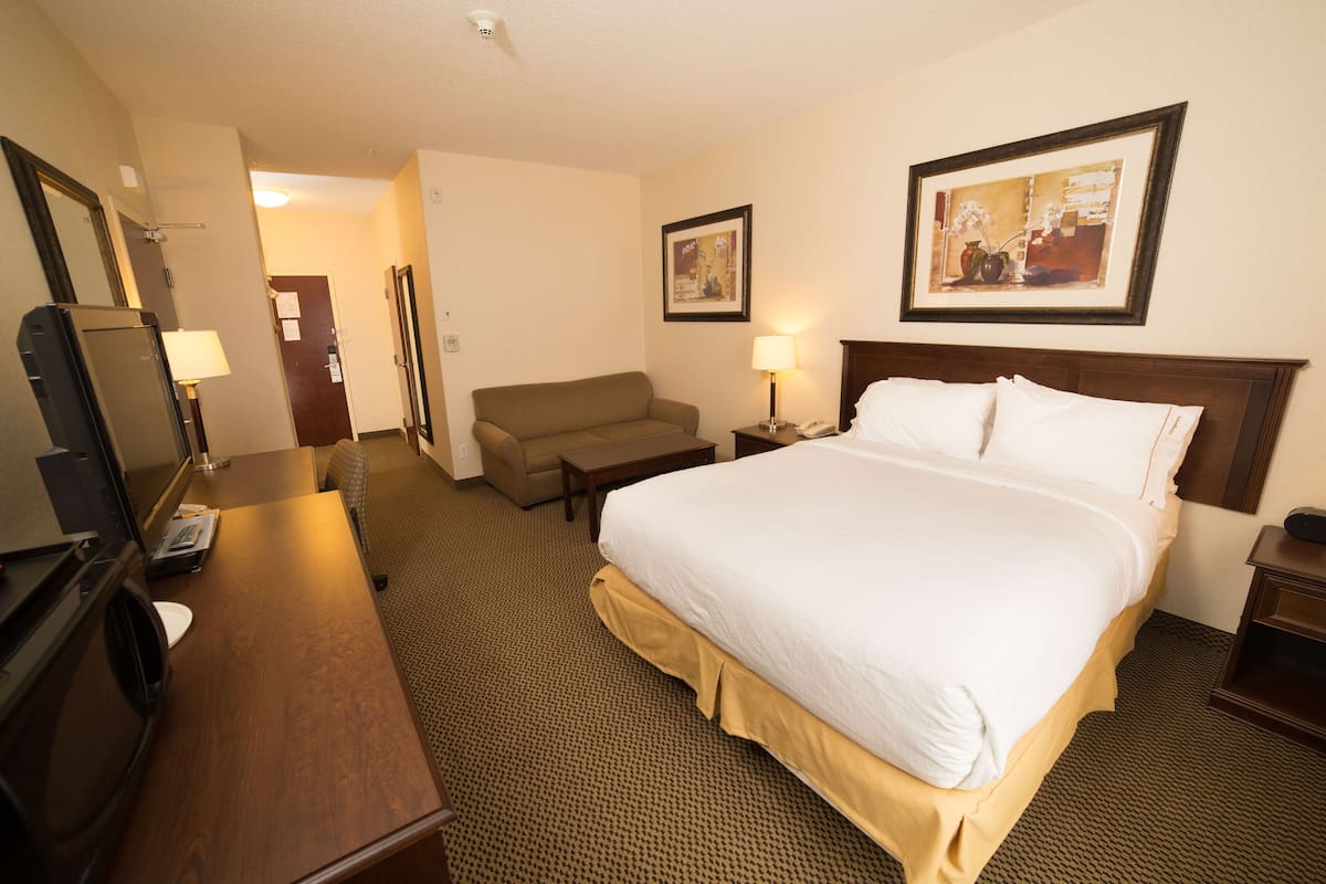 A hotel room with a bed, a desk with a computer, a chair, a lamp, and a framed picture on the wall.