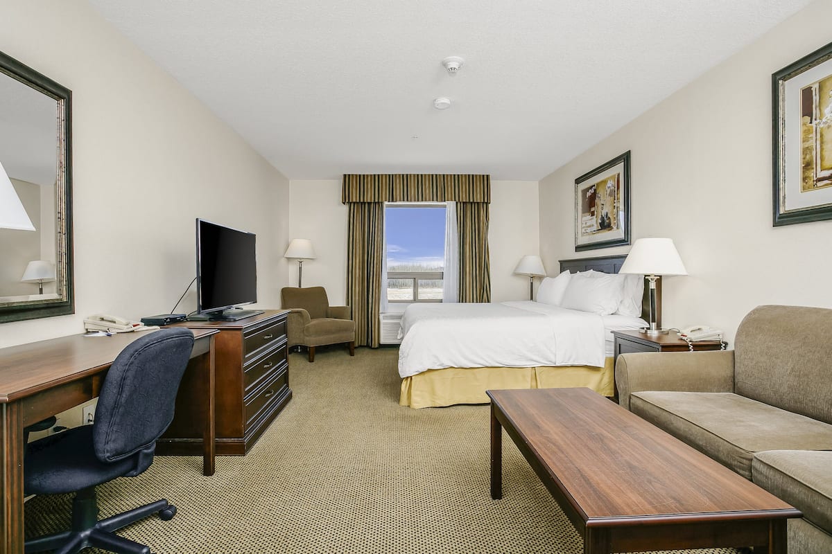 A hotel room with a bed, desk, chair, TV, and a sofa.