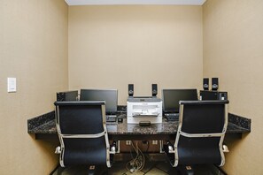 A conference room with two black office chairs, a desktop computer, a printer, and two speakers on a marble table.