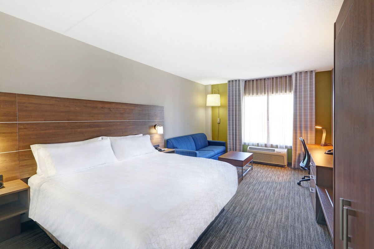 Habitación de hotel con una cama grande, un escritorio, una silla, un sofá y una ventana con cortinas.