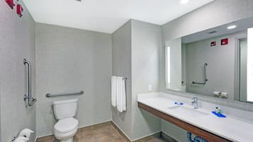 A modern bathroom with a toilet, handrails, a sink, and a mirror.