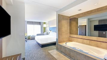 Una camera d'albergo con un letto grande, una vasca da bagno, una televisione e una finestra con tende.