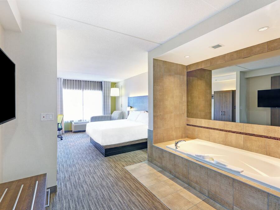 Una camera d'albergo con un letto grande, una vasca da bagno, una televisione e una finestra con tende.