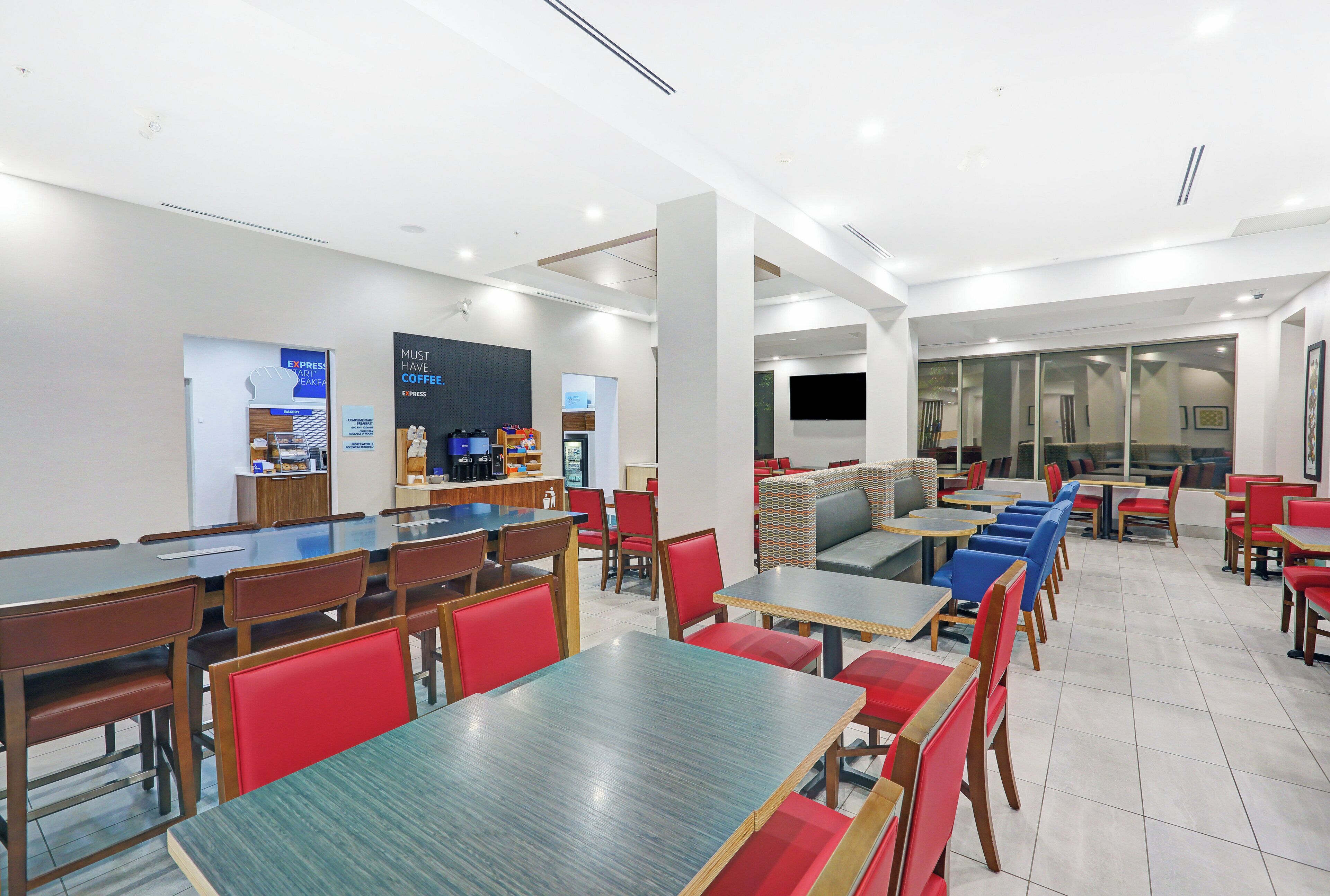 A modern dining area with multiple tables and chairs, a coffee station, and a television screen.