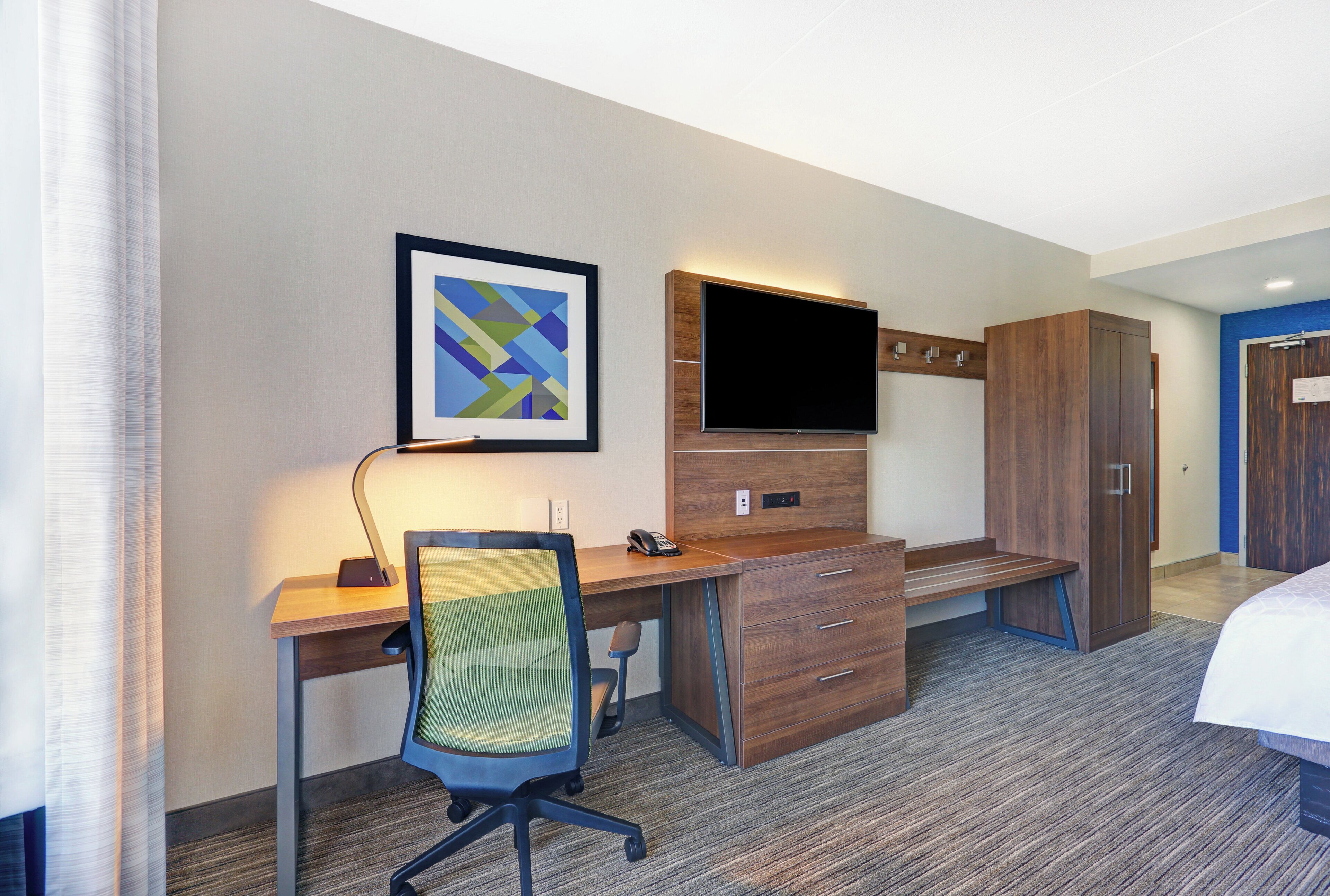A hotel room with a desk, chair, television, wardrobe, and a bed.