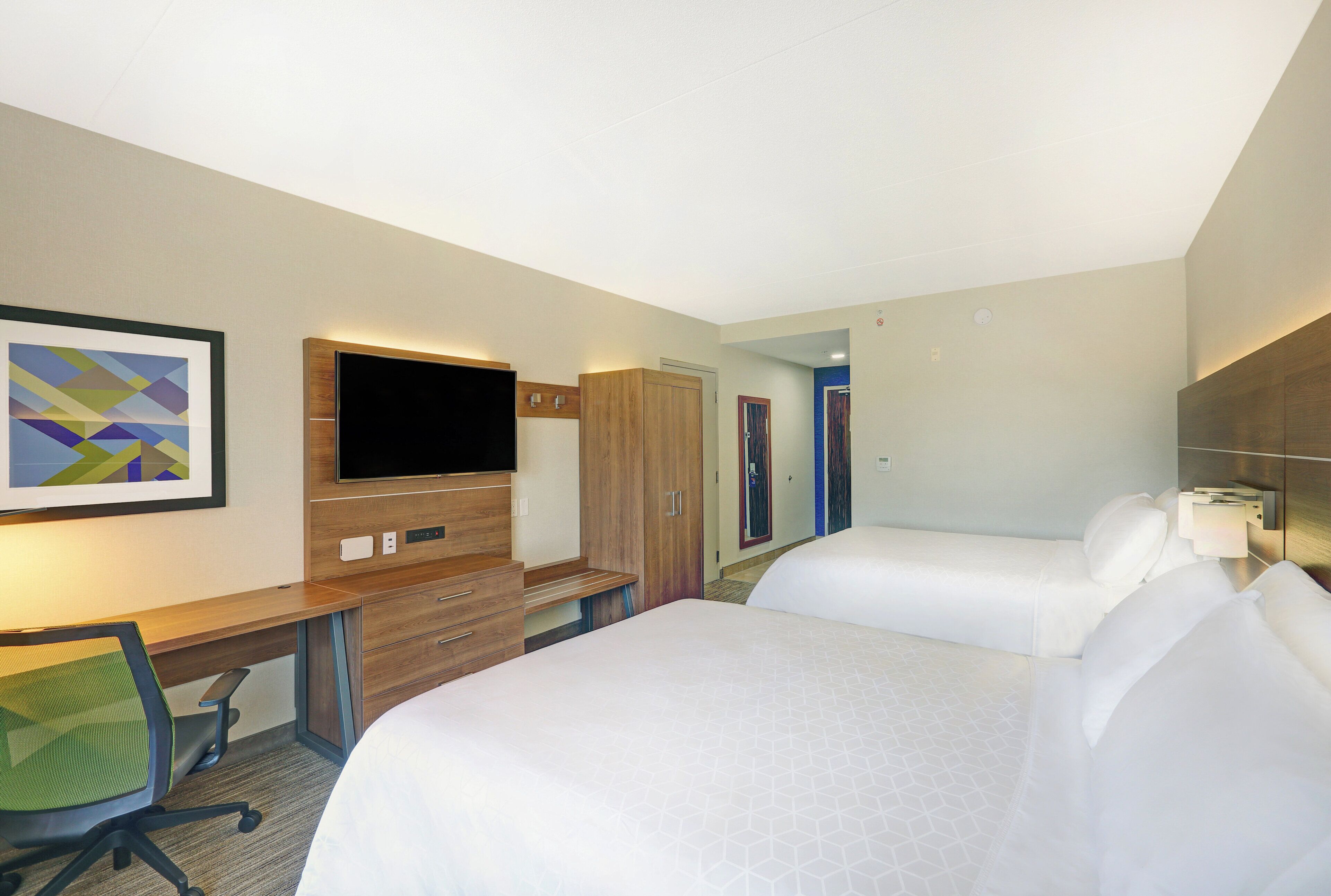A hotel room with a bed, a desk, a chair, a TV, and a wardrobe.
