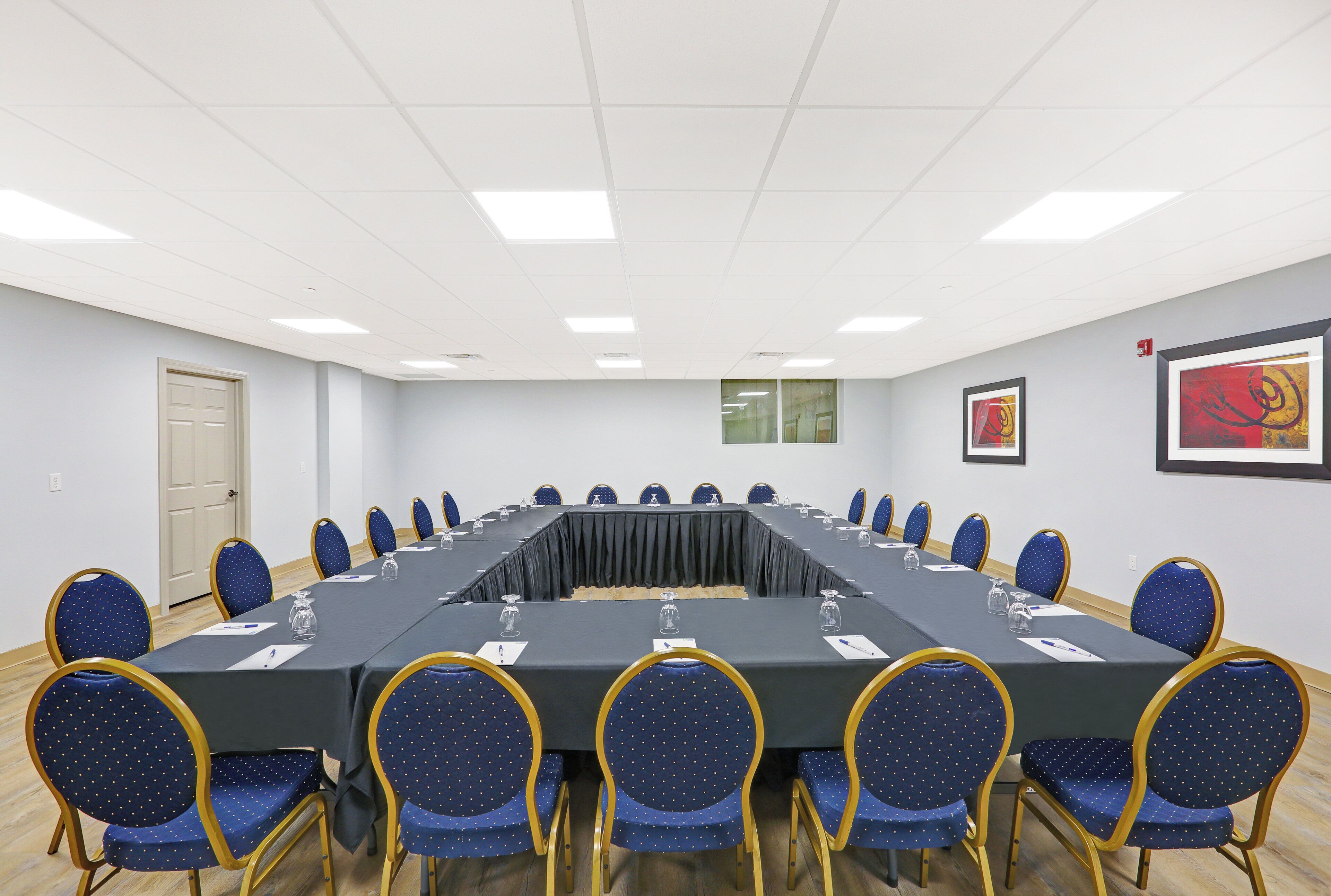 A conference room with a long table, blue chairs, and framed artwork on the walls.