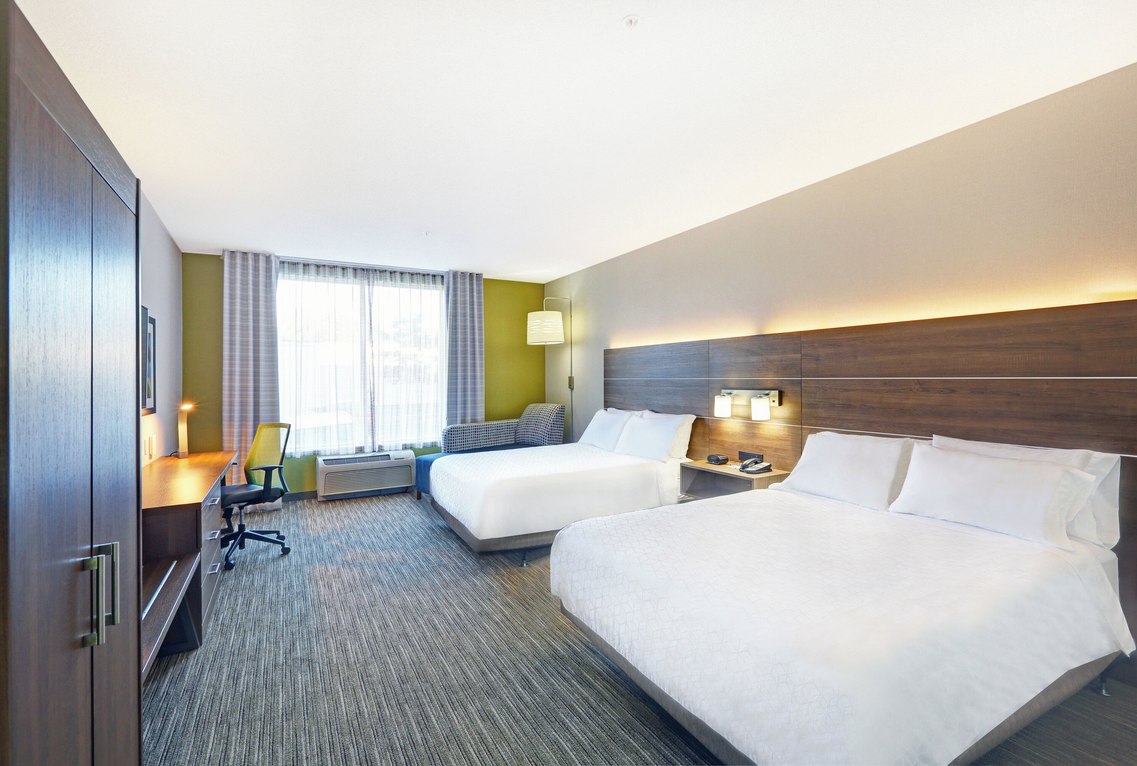 Une chambre d’hôtel avec deux lits, un bureau, une chaise, une lampe et une fenêtre avec des rideaux.