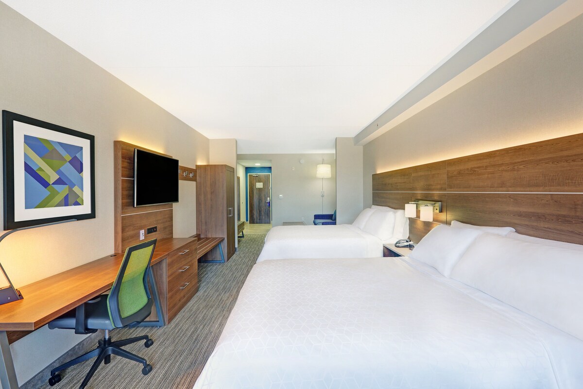 Habitación de hotel con dos camas, un escritorio, una silla, un televisor y una lámpara.
