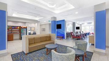 A hotel lobby with a sofa, chairs, a coffee machine, and a TV.