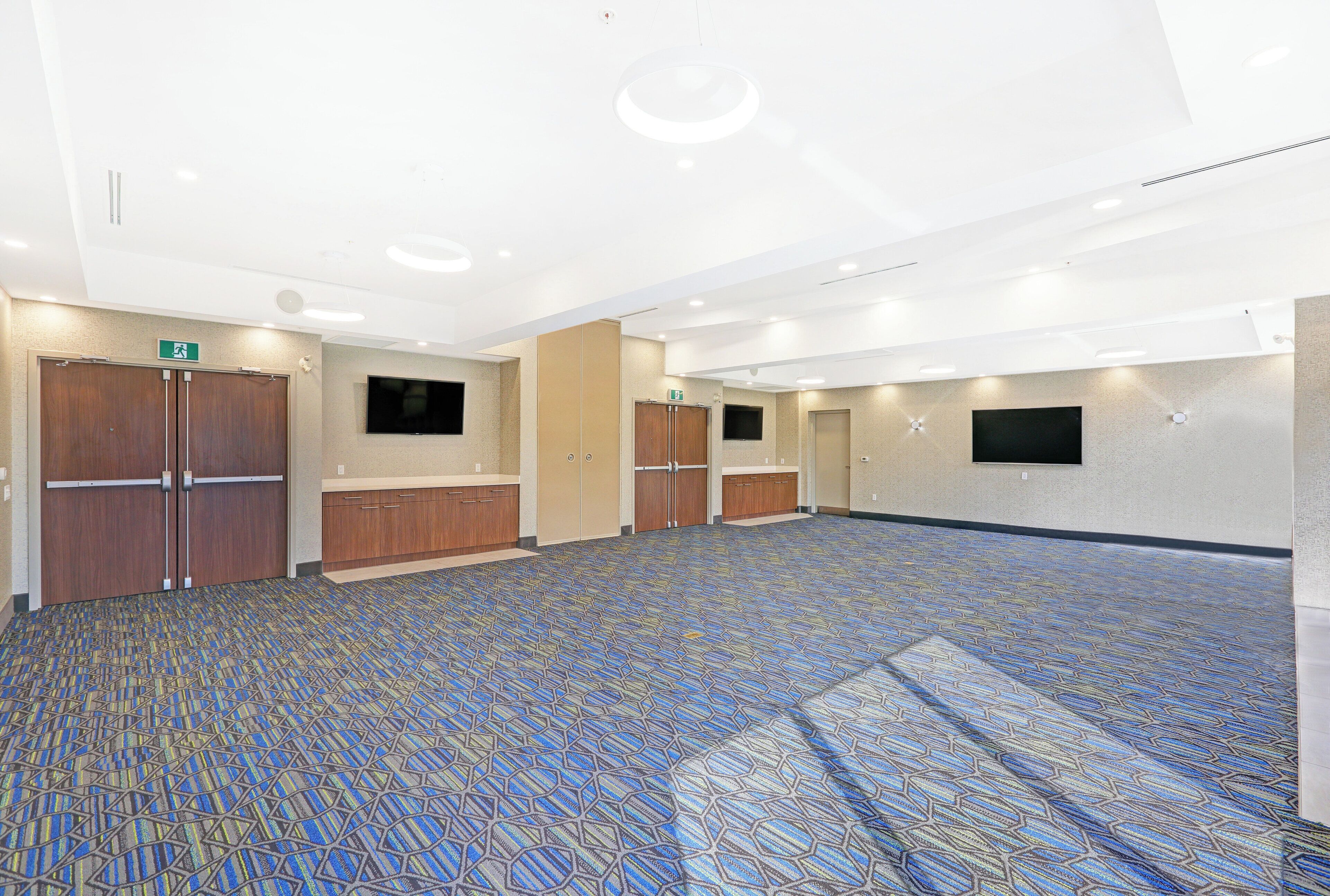 Un amplio salón de conferencias con alfombra estampada, puertas de madera e iluminación empotrada.