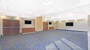 Un amplio salón de conferencias con alfombra estampada, puertas de madera e iluminación empotrada.