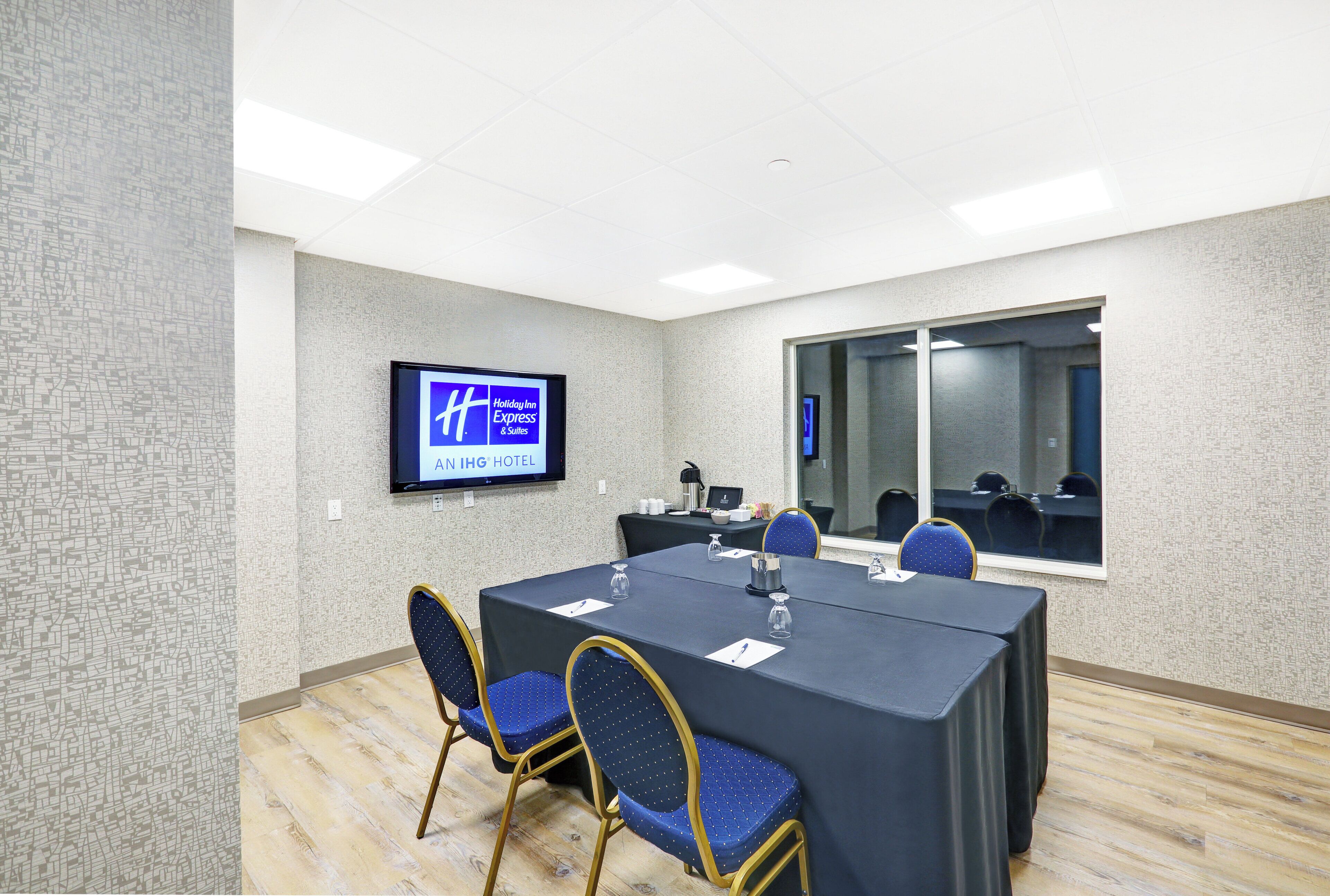 A conference room with a large table, chairs, a television screen, and a window.