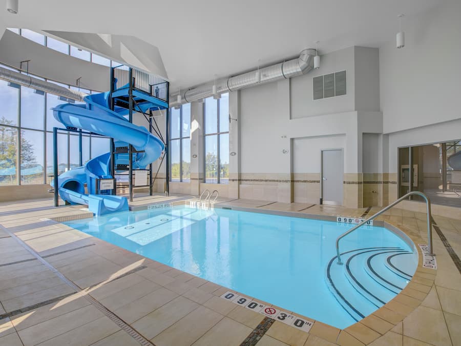 Una piscina interior con un tobogán de agua azul y una vista despejada del exterior gracias a amplias ventanas.