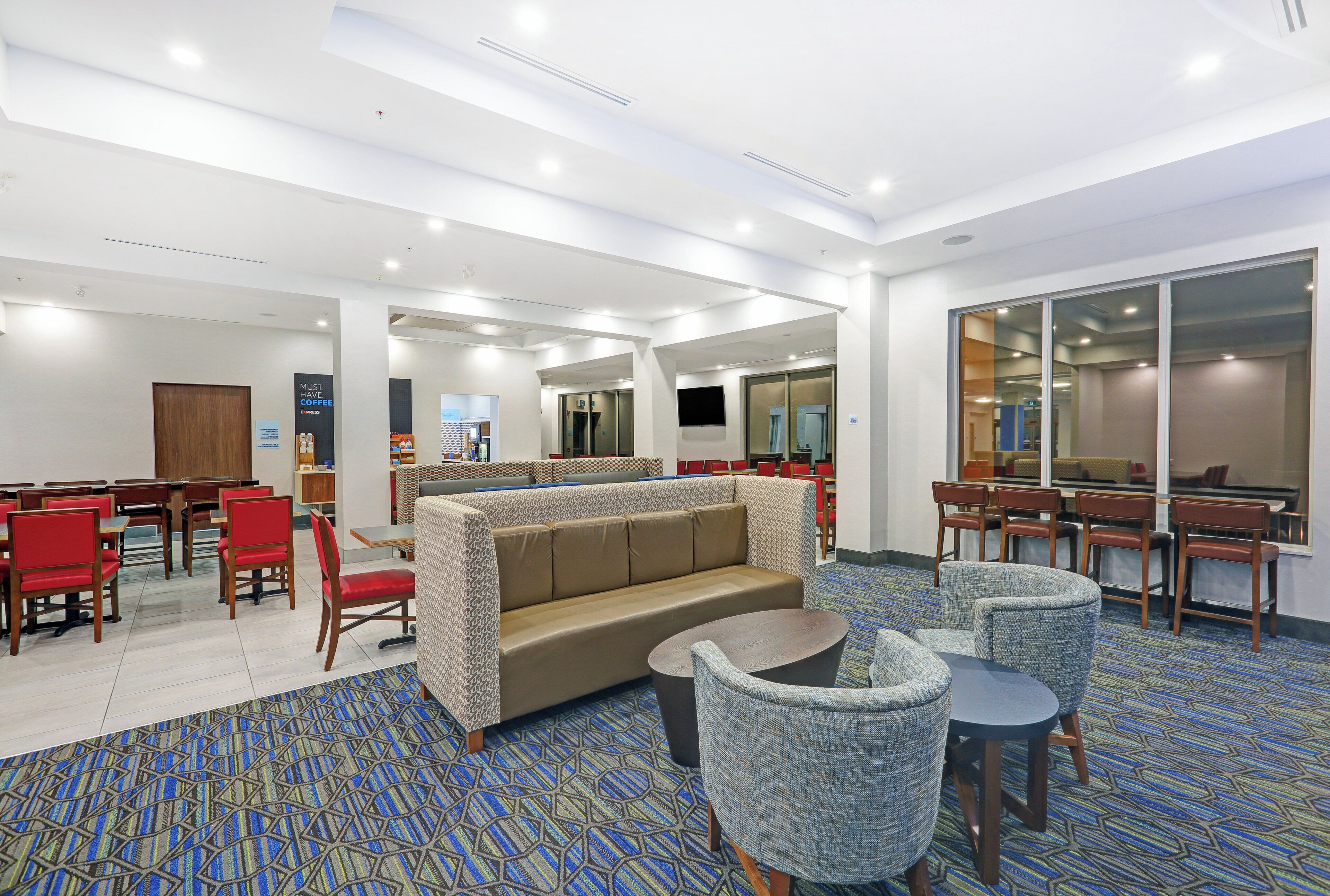 A hotel lobby with a seating area, a coffee station, and a TV screen.