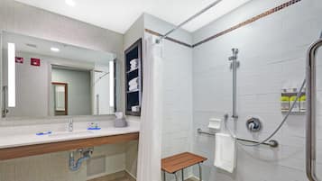 Uma casa de banho moderna com chuveiro, pia com espelho e um pequeno banco.