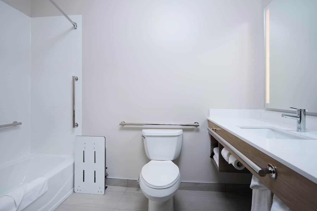 A modern bathroom with a white toilet, a bathtub, a wooden vanity with a sink, and a mirror.