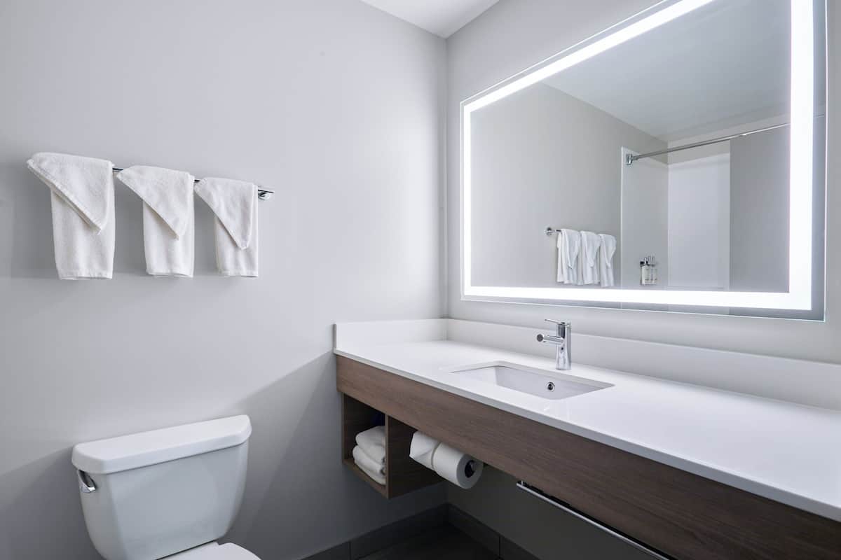 A modern bathroom with a white sink, a large mirror, and three towels hanging on the wall.