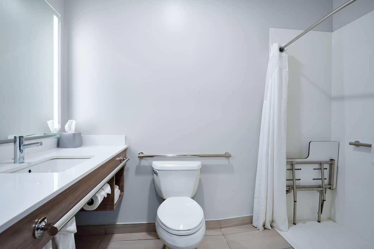 A modern bathroom with a white toilet, a sink with a wooden vanity, and a shower area with a grab bar.
