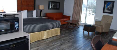 A hotel room with a bed, a sofa, a dining table, a microwave, and a refrigerator.