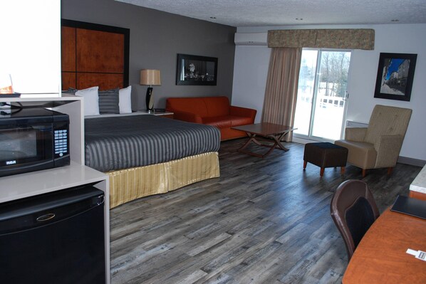 A hotel room with a bed, a sofa, a dining table, a microwave, and a refrigerator.